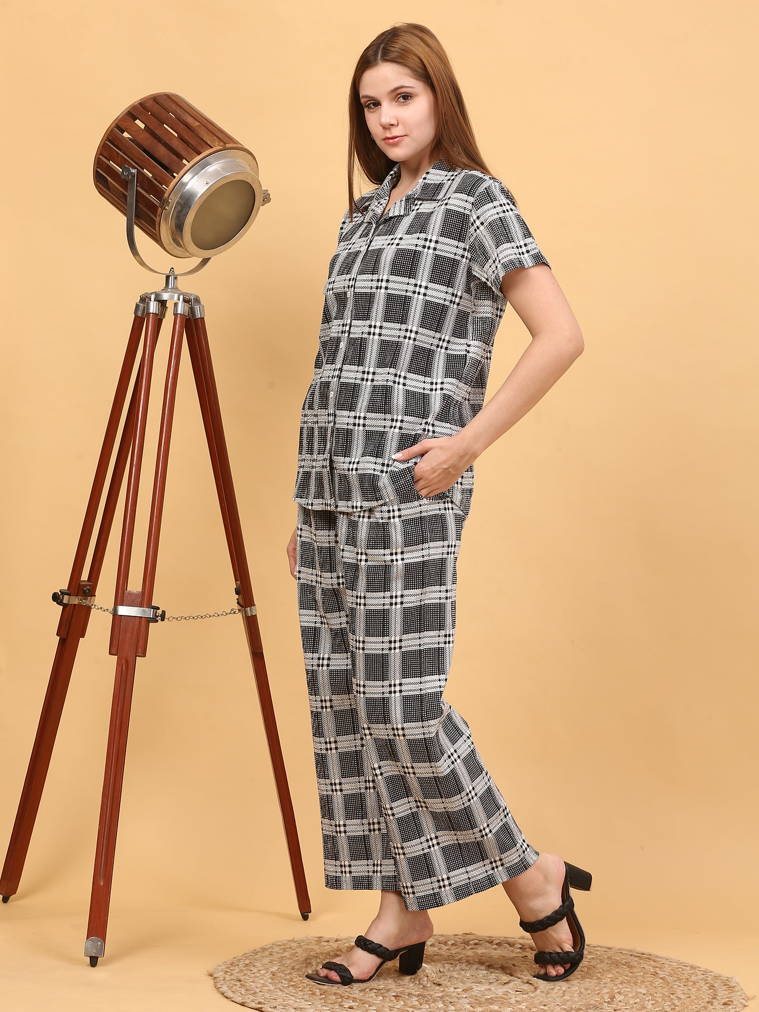 Woman wearing a checkered outfit standing next to a wooden floor lamp on a beige background